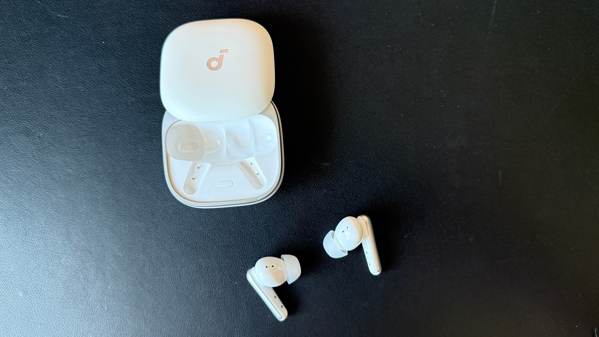 The Soundcore Liberty 5 earbuds, on a black leather desktop.