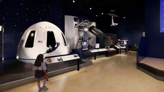 a woman walks past a white space capsule in a dark-walled museum hall