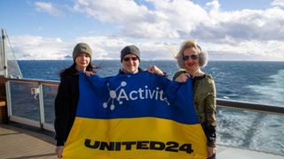 three people hold up a blue and yellow flag on the deck of a ship at sea