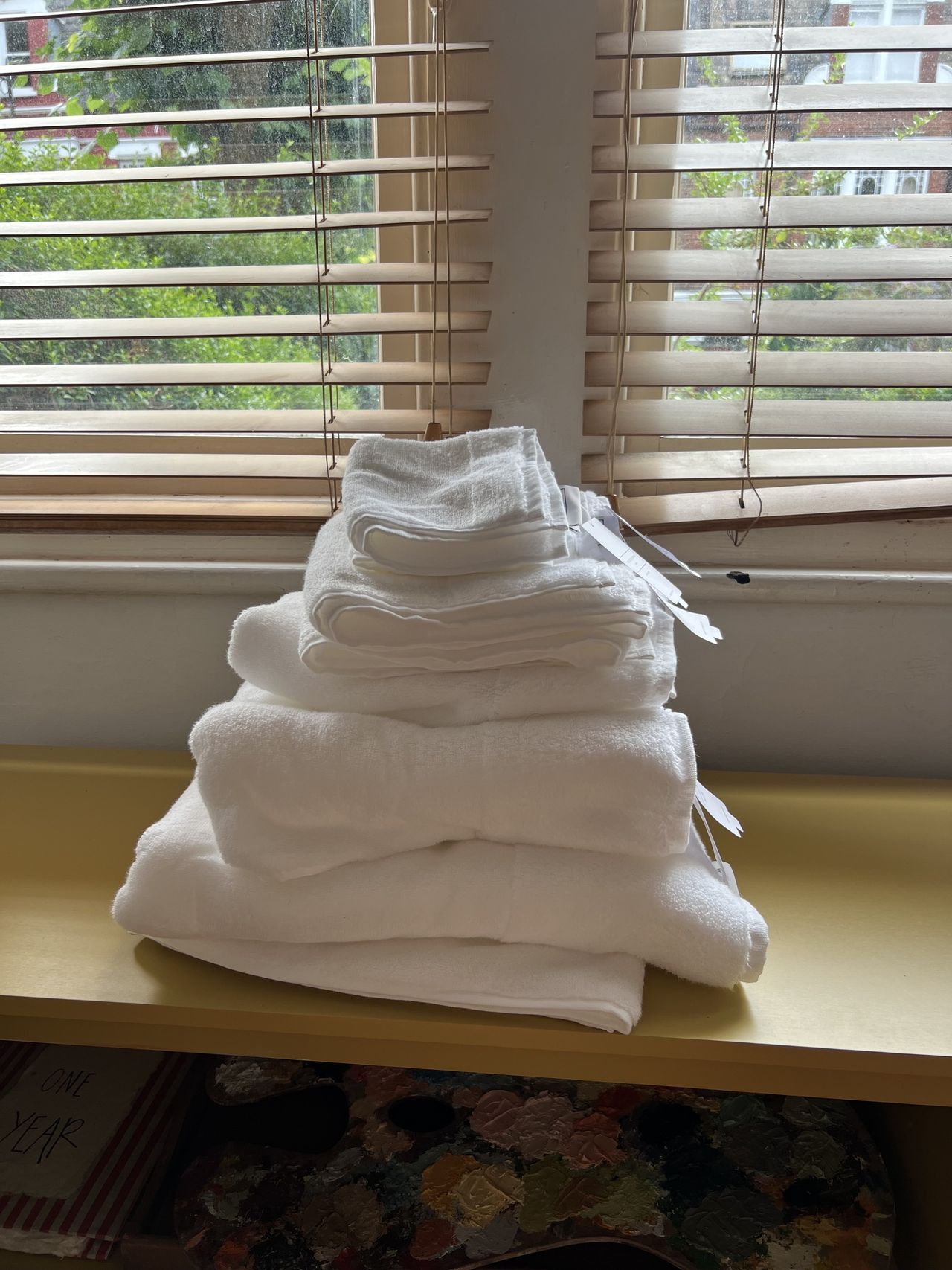 Image of a stack of white towels sitting on a yellow console in front of a window.