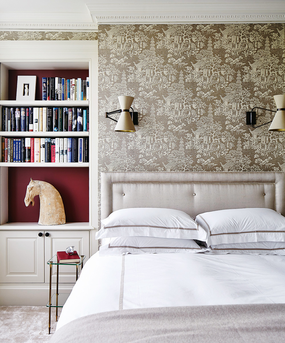 A bed with a silk headboard next to a bookshelf