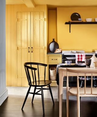 Yellow painted kitchen with wooden dining table, gray flooring, black shelving