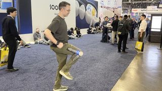 Tom's Guide Senior Writer Dan Bracaglia demoing the power pants on the show floor with folks milling about around him; he's flexing his right leg