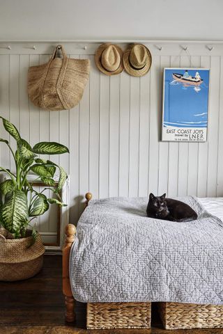 A black cat sat on a bed in front of a wood panelled wall with pegs