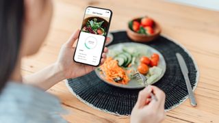 Woman eating salad and tracking calories through an app, part of reverse dieting