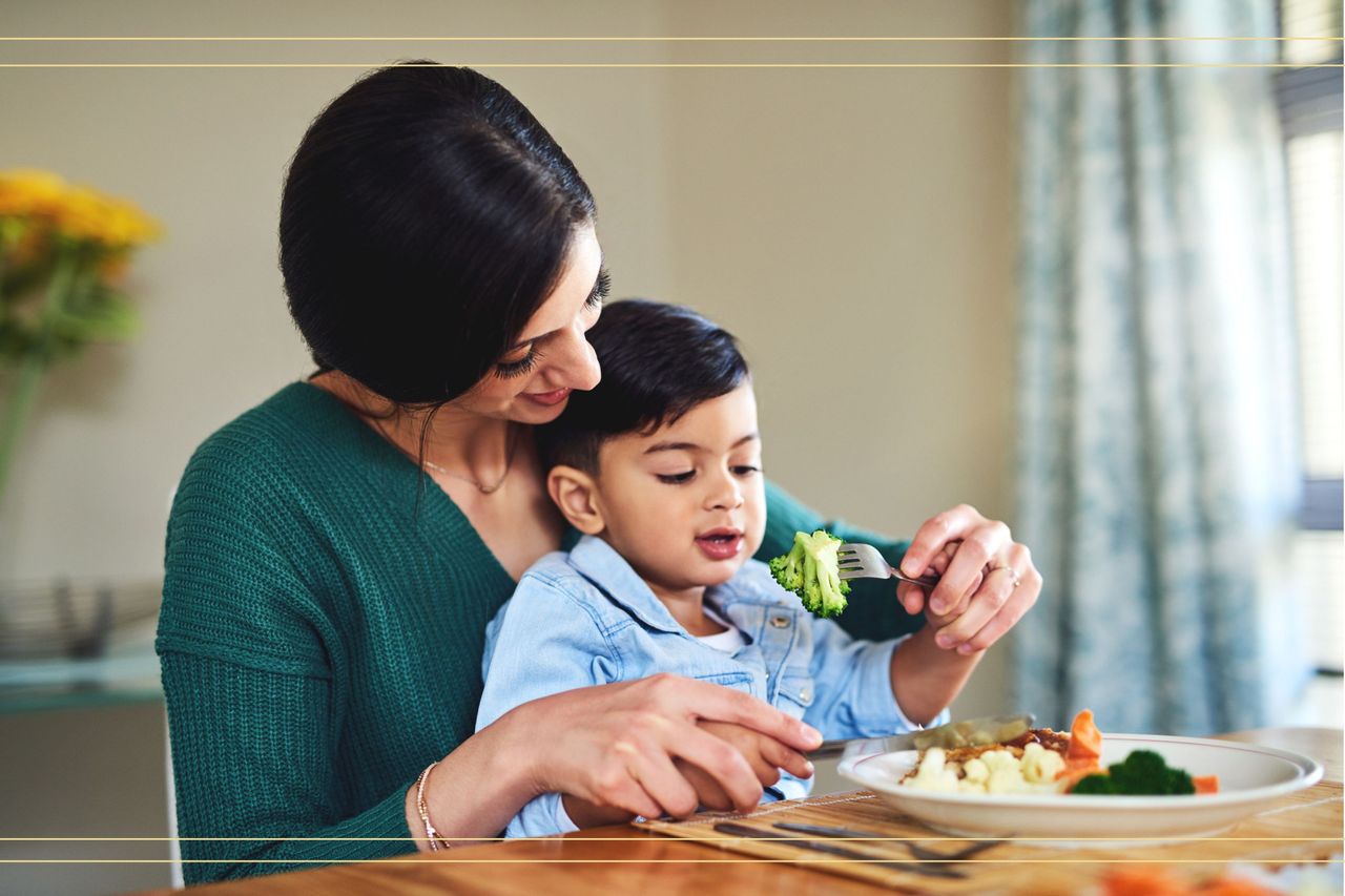 Mum with child on her lap broccoli on a fork encouraging him to eat it and smiling