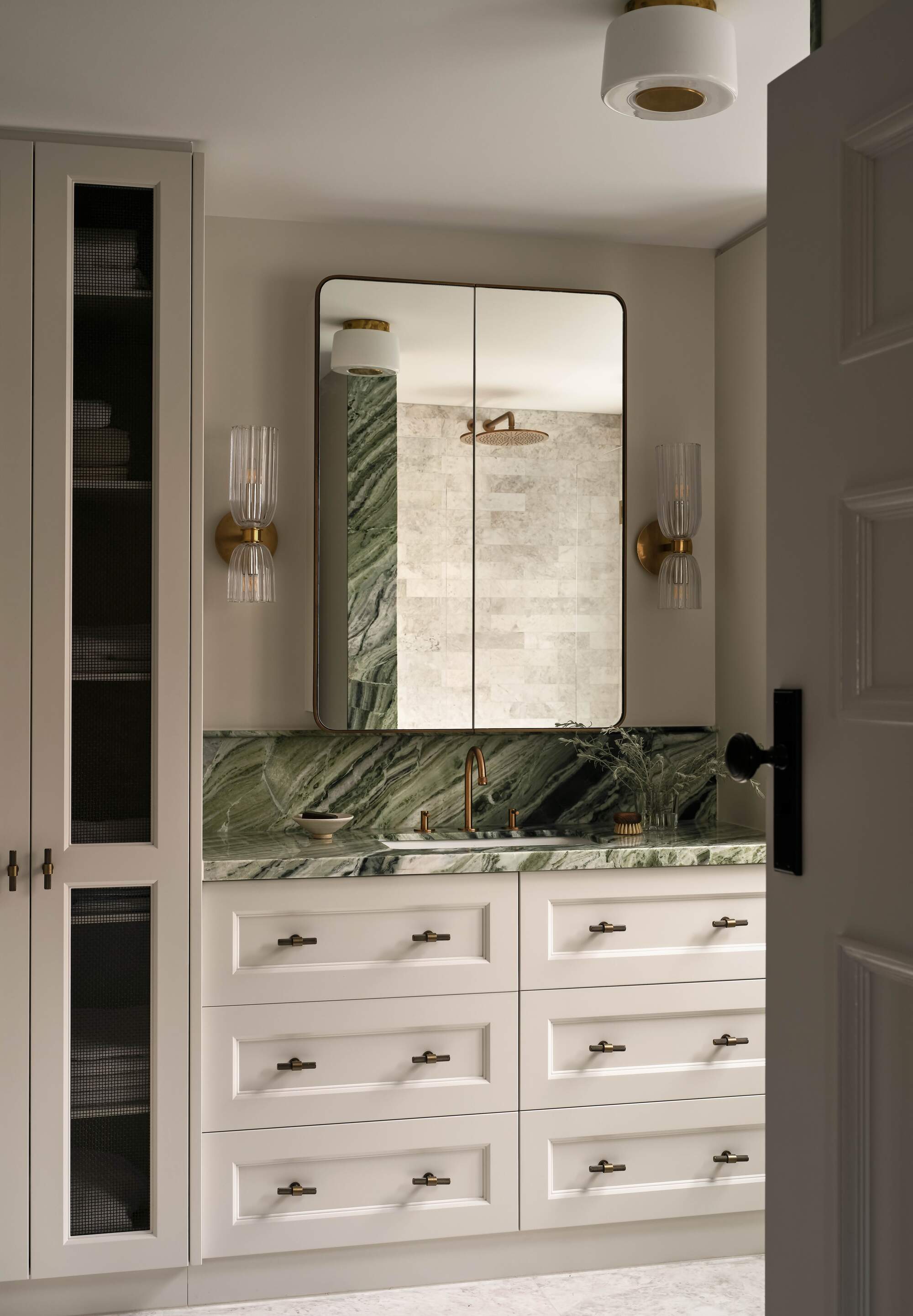 modern bathroom with white shaker cabinet with drawers, a built-in cupboard, green marble vanity with medicine cabinet above and two wall sconces on either side
