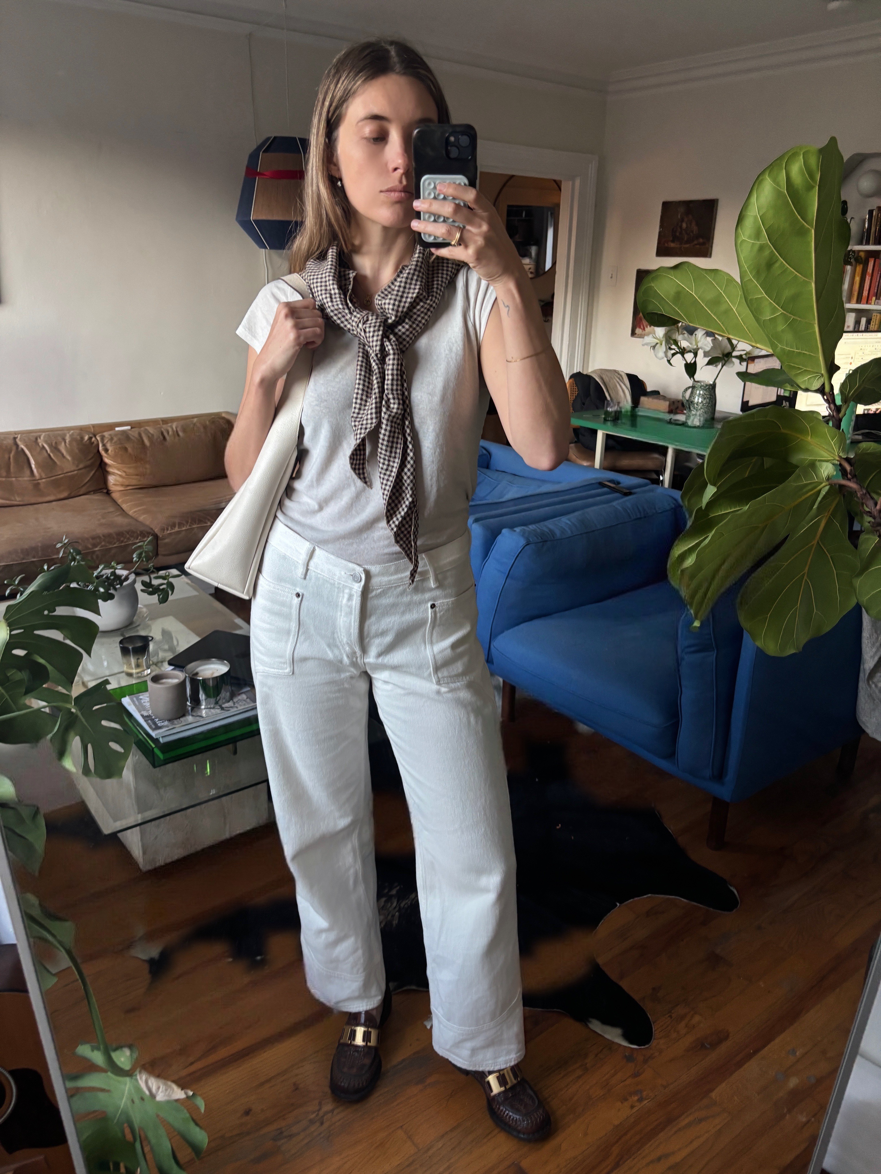 Aemilia Madden taking a selfite in white jeans, white tee, a gray scarf, and brown shoes