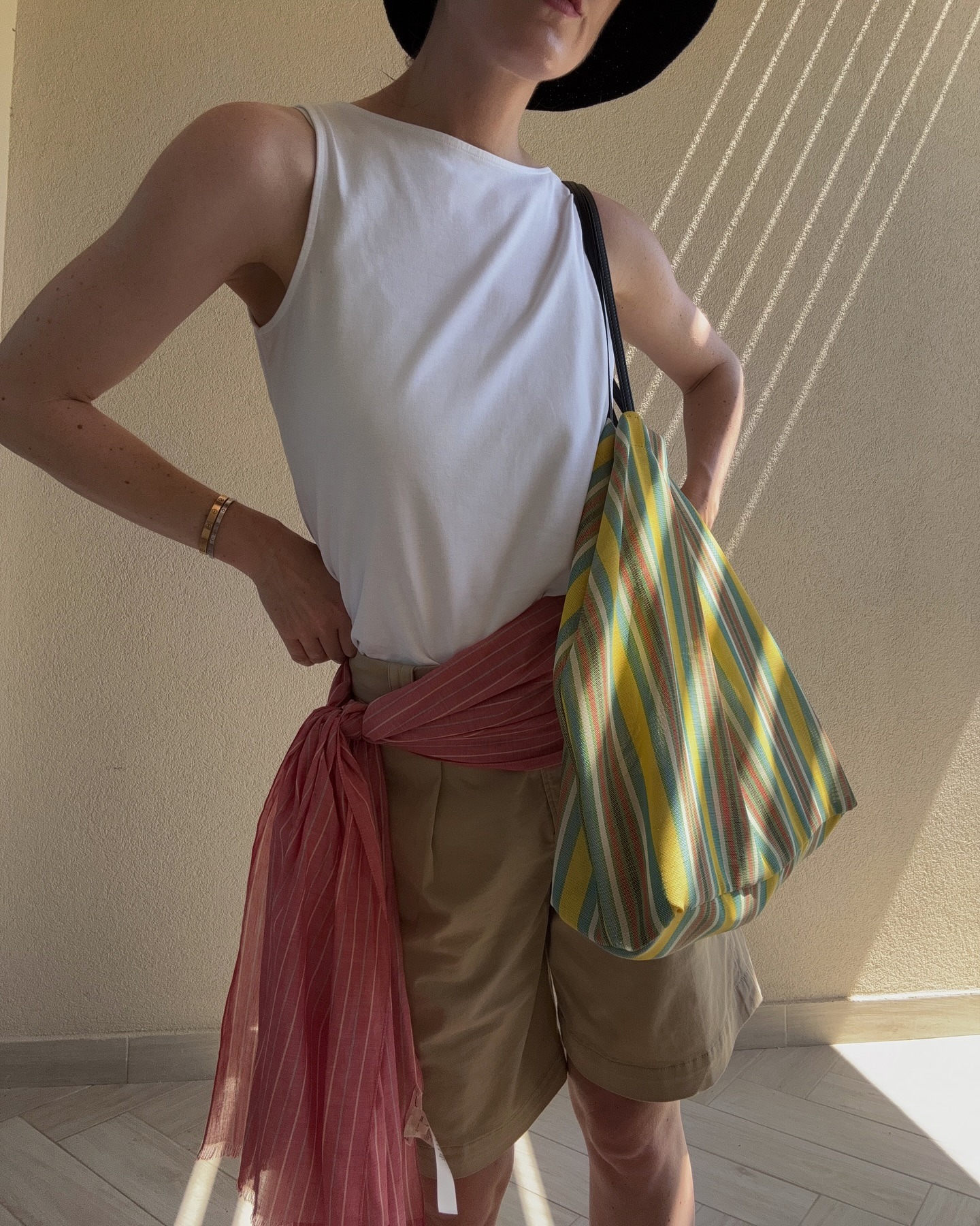 Influencer wearing white tank, khaki shorts, red waist scarf, and striped The Row mesh market tote.