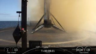 A black and white spacex falcon 9 rocket first stage sits on the deck of a ship at sea.