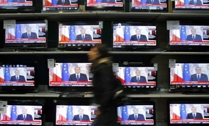 A woman walks past television screens showing Silvio Berlusconi's farewell speech Sunday: The controversial leader may be gone, but it won't be for long, say critics.
