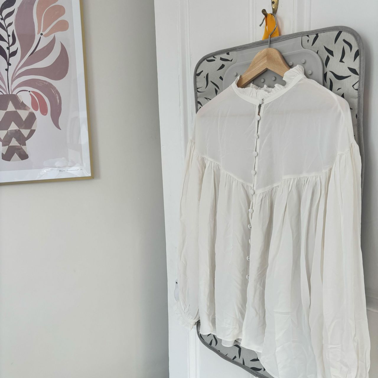 wrinkled blouse hanging on a door with artwork on wall