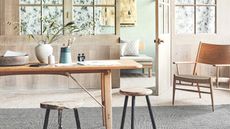 Dining room with wooden table, chair and stools on a grey rug and wooden clad and green walls.