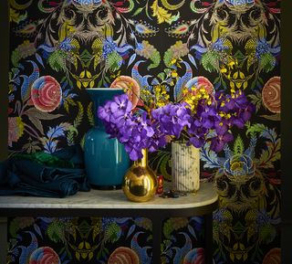 purple flowers and vases on a shelf with patterned wallpaper