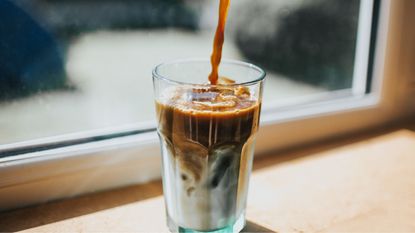 how to make iced coffee from hot coffee: a glass of iced coffee being poured over ice
