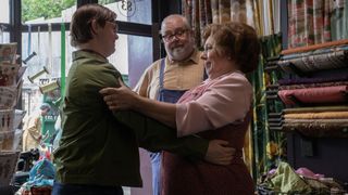 Daniel Laurie in a green shirt as Reggie is embraced by Annabelle Apsion in a pink top as Violet as Cliff Parisi in dungarees as Fred looks on in Call the Midwife.