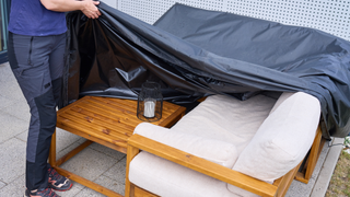 person covering a garden sofa and table with a black cover 