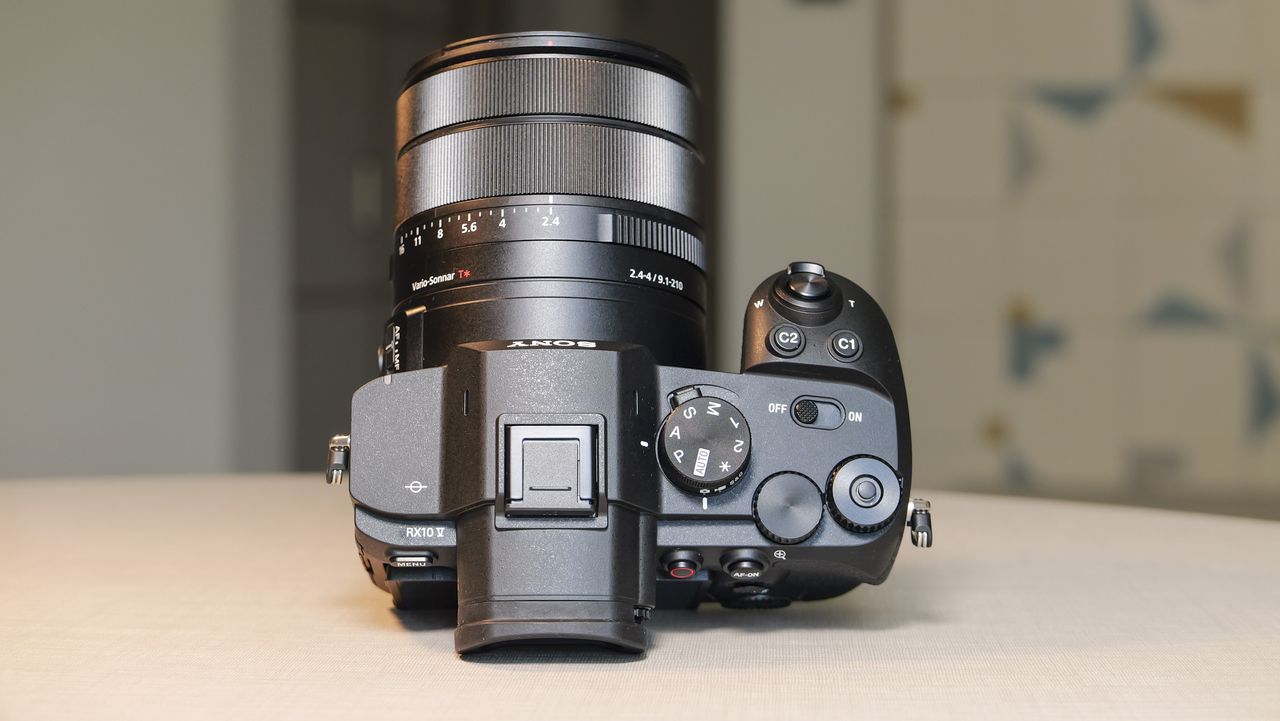 The Sony RX10 V bridge camera on a white table with a patterned wallpaper background, it's pointing upwards and we can see the top of the camera