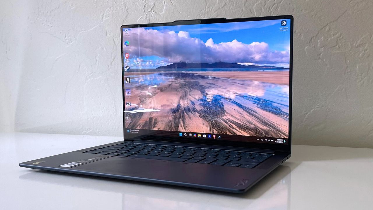 An open and powered on black laptop sitting on a white desk, showing a desert landscape with clouds and blue sky on its screen.