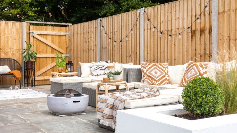 Outdoor space with wooden fencing and gate, and outdoor lounge set-up with boho cushions, brazier and festoon lights