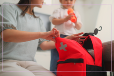 Woman looking in first aid bag with young daughter in background