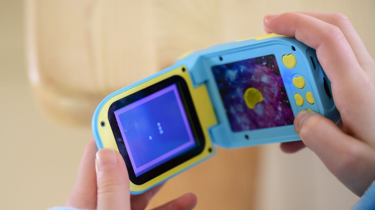 Cheap blue kids camera on a table with screen flipped out and games being played
