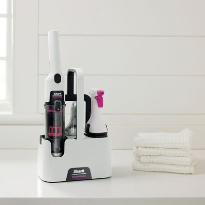 Shark Stainforce Spot Cleaner HX100UKT on a white table next to four white face towels stacked on top of each other