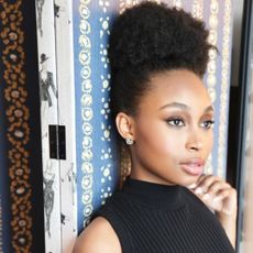 broadway ragtime actress nichelle lewis leans against a printed wall and looks off in the distance styled in a black dress with her hair up