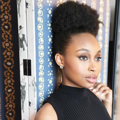 broadway ragtime actress nichelle lewis leans against a printed wall and looks off in the distance styled in a black dress with her hair up