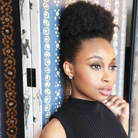 broadway ragtime actress nichelle lewis leans against a printed wall and looks off in the distance styled in a black dress with her hair up