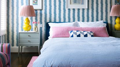 pink and blue bedroom with striped wallpaper and large bedside lamp
