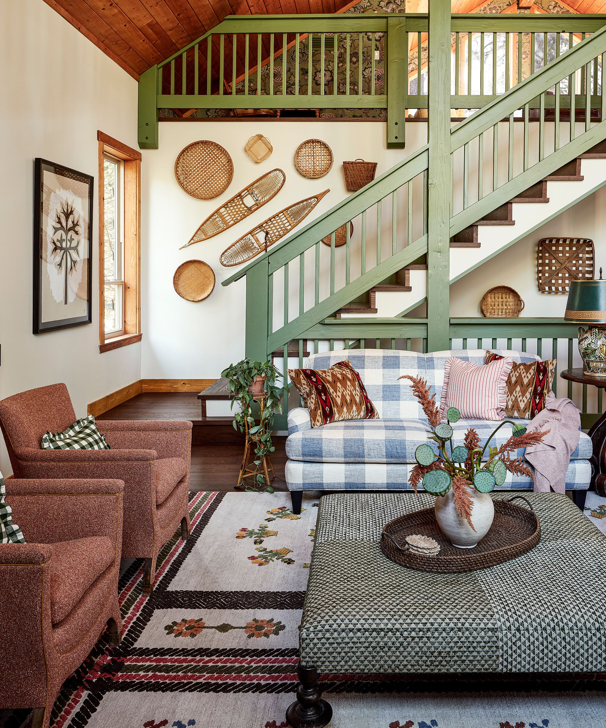 a large vaulted great room in a ski house with folk country decor with a large green painted staircase and a collection of vintage baskets on the wall