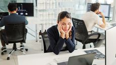 A woman sitting at her desk at work looks tired and unmotivated.