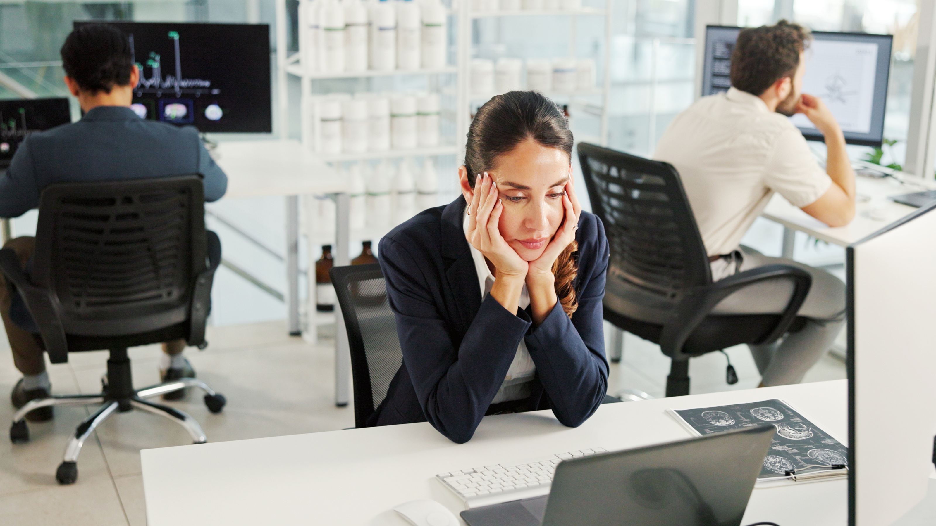 A woman sitting at her desk at work looks tired and unmotivated.