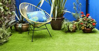 Small courtyard garden with artificial grass with a woven chair and potted plants