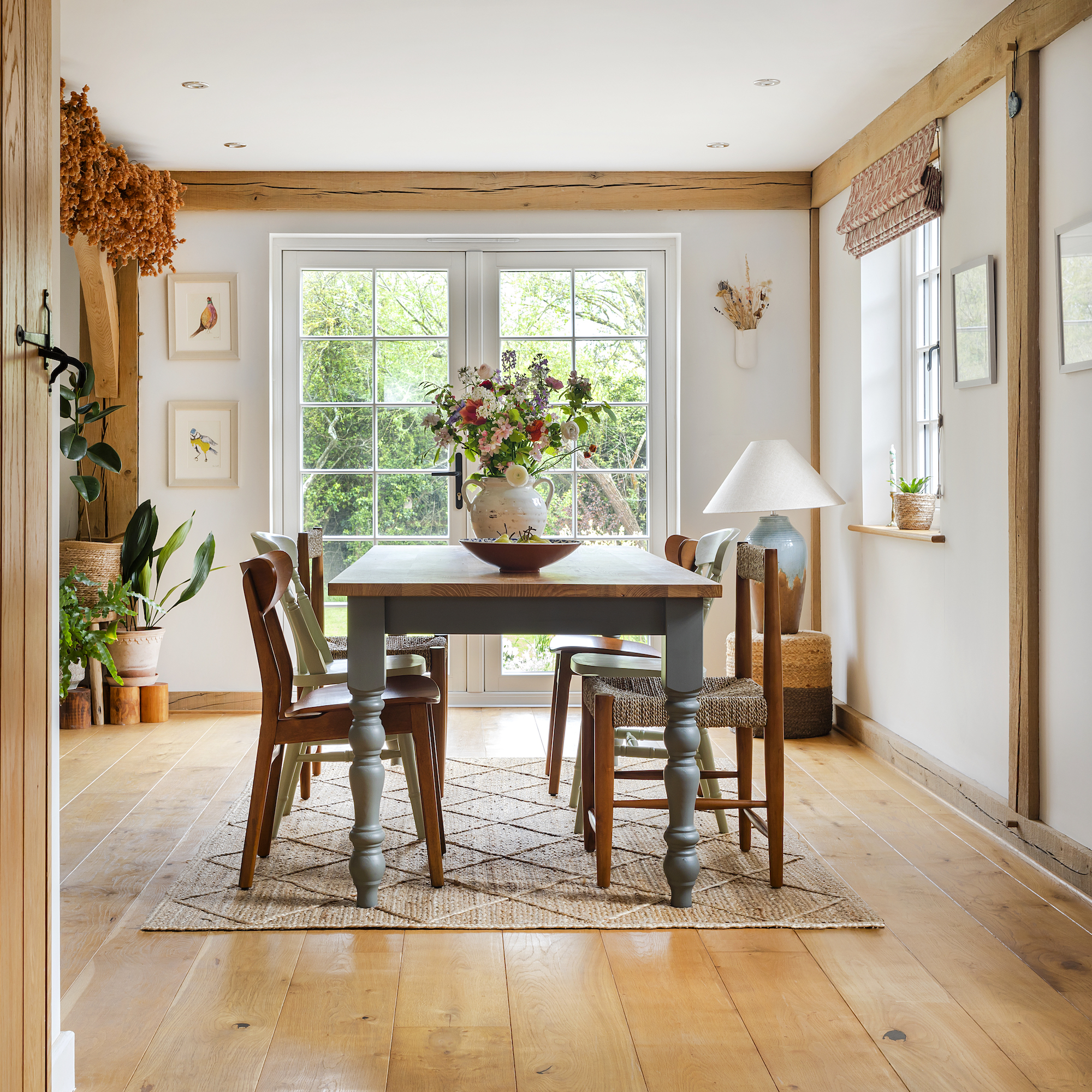 dining room in oak frame house with farmhouse table and mismatched chairs and patio doors onto garden