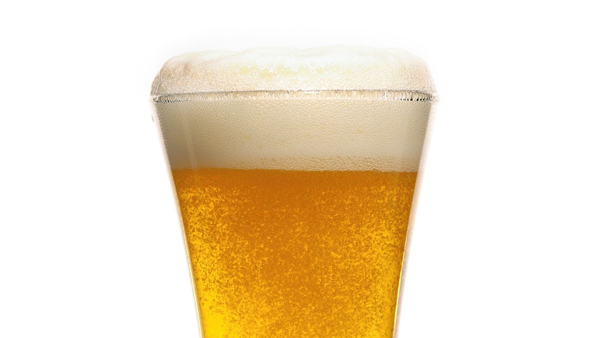 A close-up of a glass of beer shows rising bubbles and a foamy head.