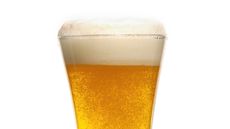 A close-up of a glass of beer shows rising bubbles and a foamy head.