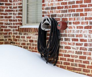 A hose in winter next to a faucet cover