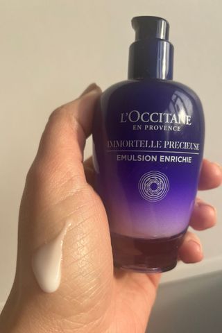 a hand holding loccitane immortelle cream with a smear of product