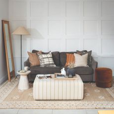 A white living room with wall panelling and a dark grey sofa on a jute rug