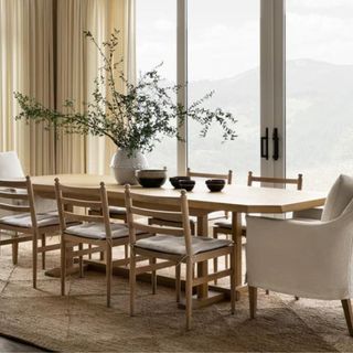 A wooden dining table with eight chairs in a room with floor to ceiling windows