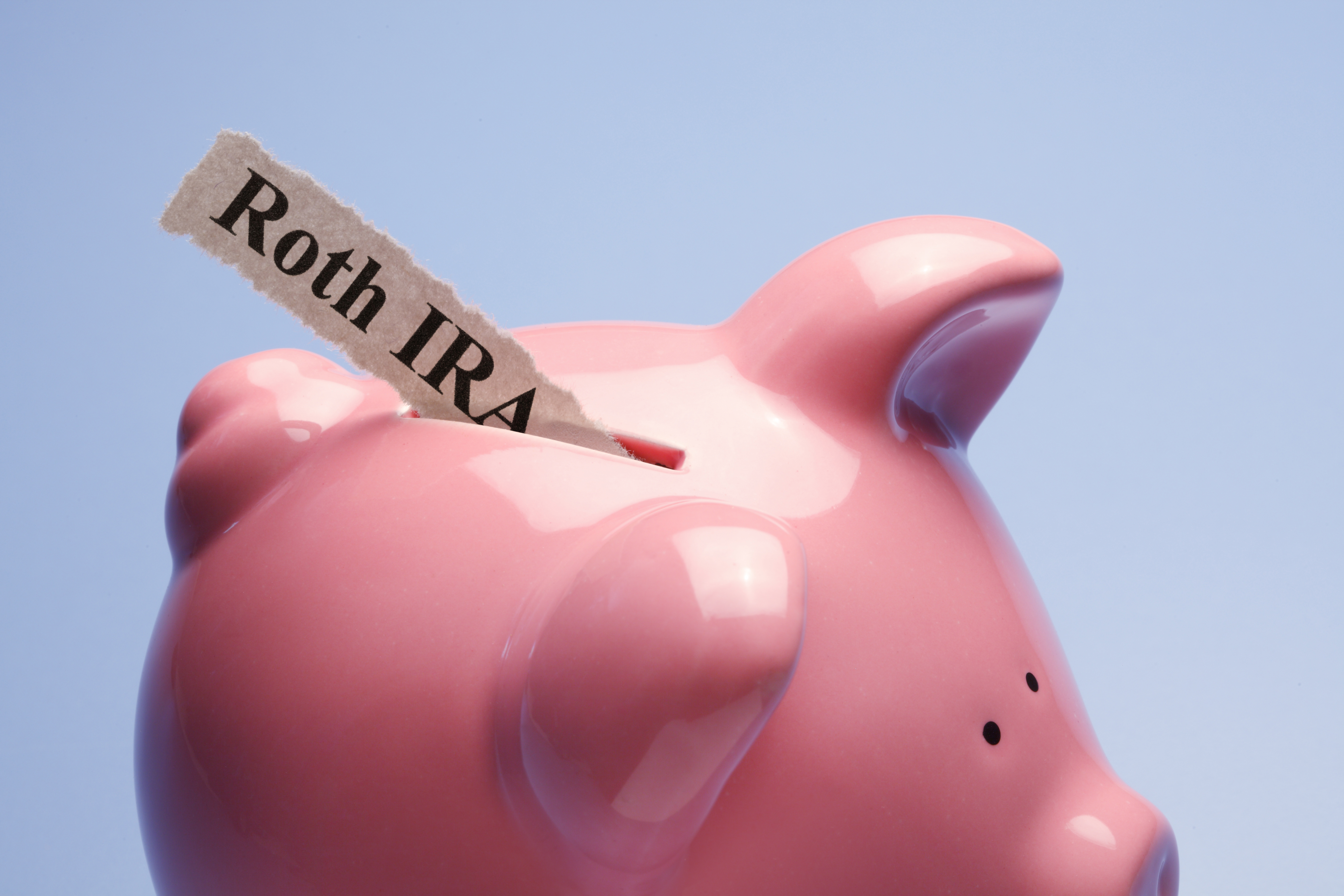 "Retirement" is printed on a torn piece of paper that is inserted into the coin slot of a pink piggy bank against a blue background.