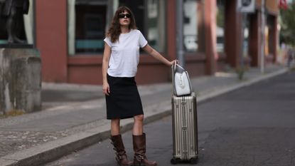 Lea Naumann is seen wearing black sunglasses from Prada, a white tee from Mother Denim, a black knee-length vintage skirt, brown leather boots with silver buckle closure from Miu Miu, a white leather Supernova bag from Prada and a silver suitcase from Rimowa on July 11, 2023 in Berlin, Germany.