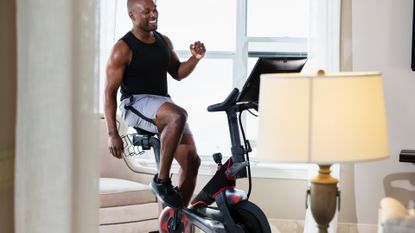 A black rider is on a Peloton bike in a lounge with a large lap in the foreground 