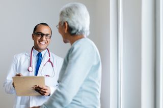 Doctor with red stethoscope and clipboard smiles at a female patient