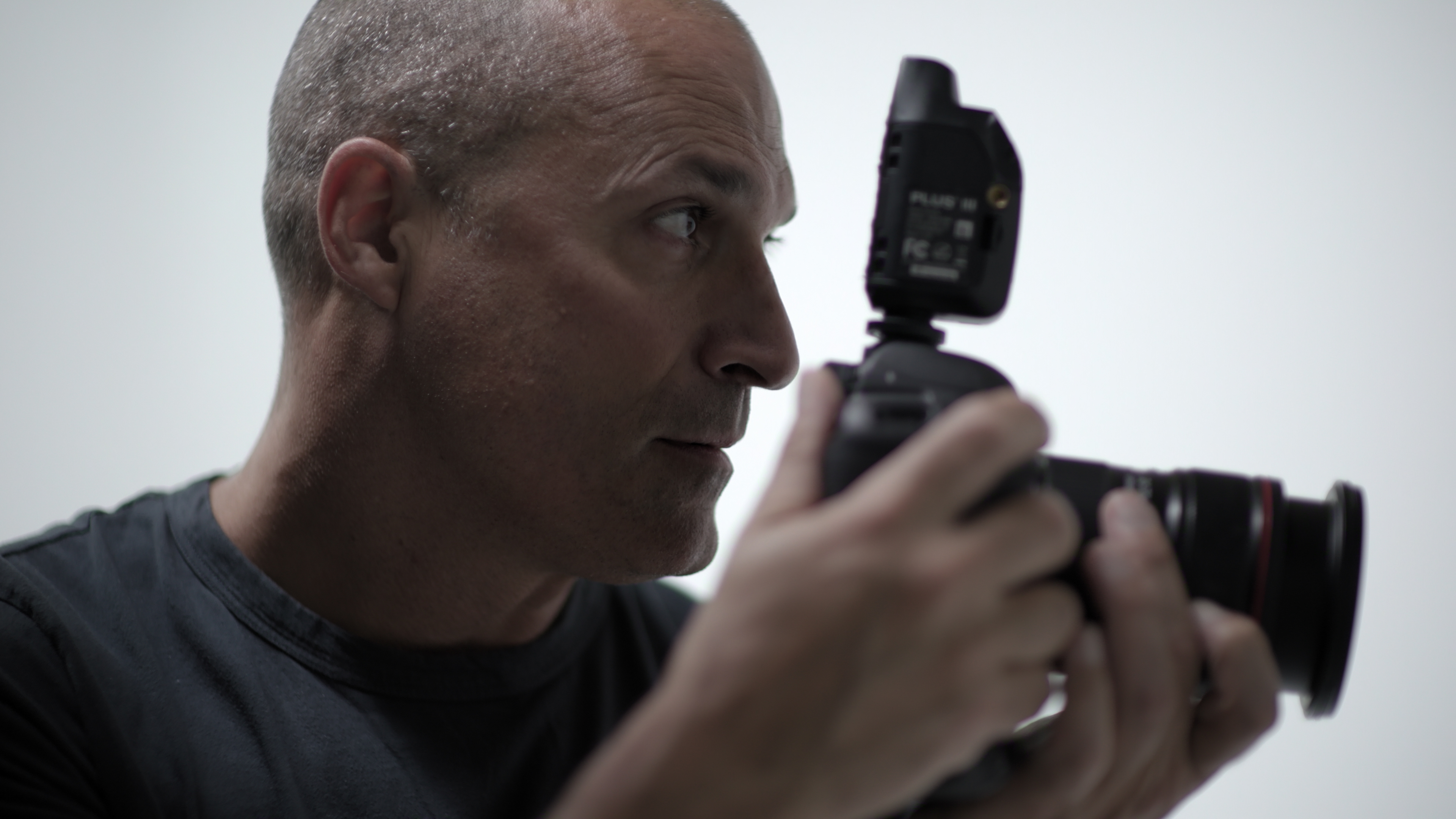 Photographer Nigel Barker is seen in side profile as he holds a DSLR camera up to take a photo, in the Netflix docuseries 'Reality Check: Inside America's Next Top Model.'