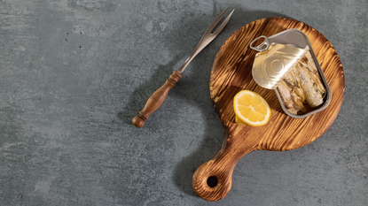 Tinned sardines on wooden board with a slice of lemon
