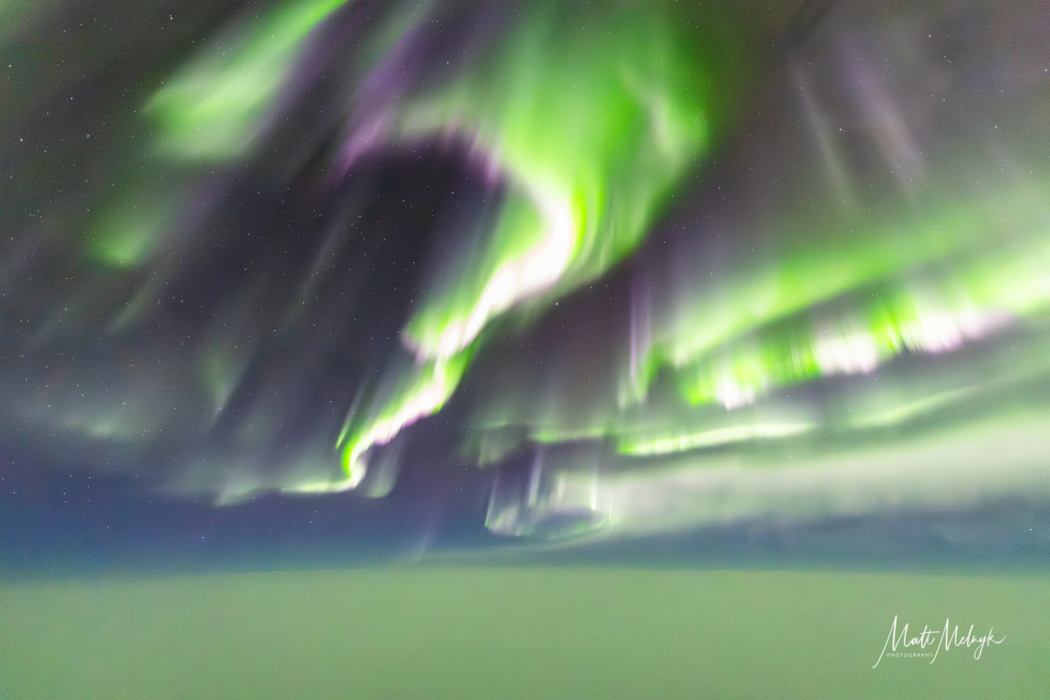 curtains of green auroras fill the sky, with a blanket of cloud below.