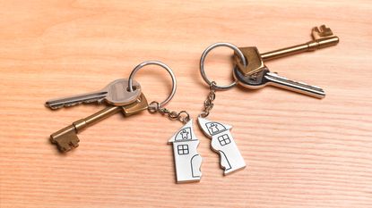 Two sets of keys sharing one key chain shaped like a house that's split in half.